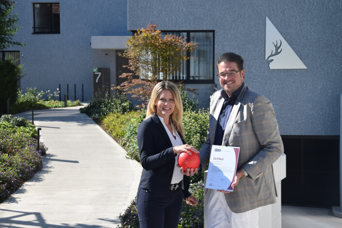 Patrizia Eckenstein, Mitglied des Verwaltungsrats und Fabian Eckenstein, Geschäftsführer mit dem iPunkt-Zertifikat. Im Hintegrund ist das Firmengebäude und das Unternehmens-Logo zu sehen. 