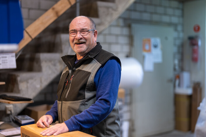 Manuel Martin steht lachend und im Arbeitsoverall im Lager der Gloor Rehabilitation & Co. AG