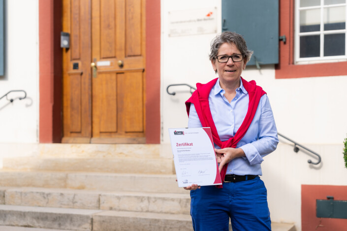 Caroline Rietschi steht vor dem Eingang der Gemeindeverwaltung mit dem iPunkt-Zertifikat in der Hand.
