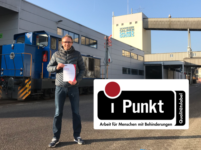Tanguy Quartnenoud, HR-Bereichsleiter und iPunkt-Beauftragter posiert mit dem iPunkt-Zertifikat auf dem Areal Saline Riburg der Schweizer Salinen AG. Das iPunkt-Logo ist auf dem Foto eingefügt.